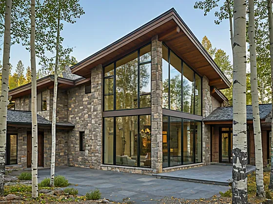 Luxury mountain estate architecture with large glass windows and stone facade nestled in aspen trees in Mountain Village, Colorado
